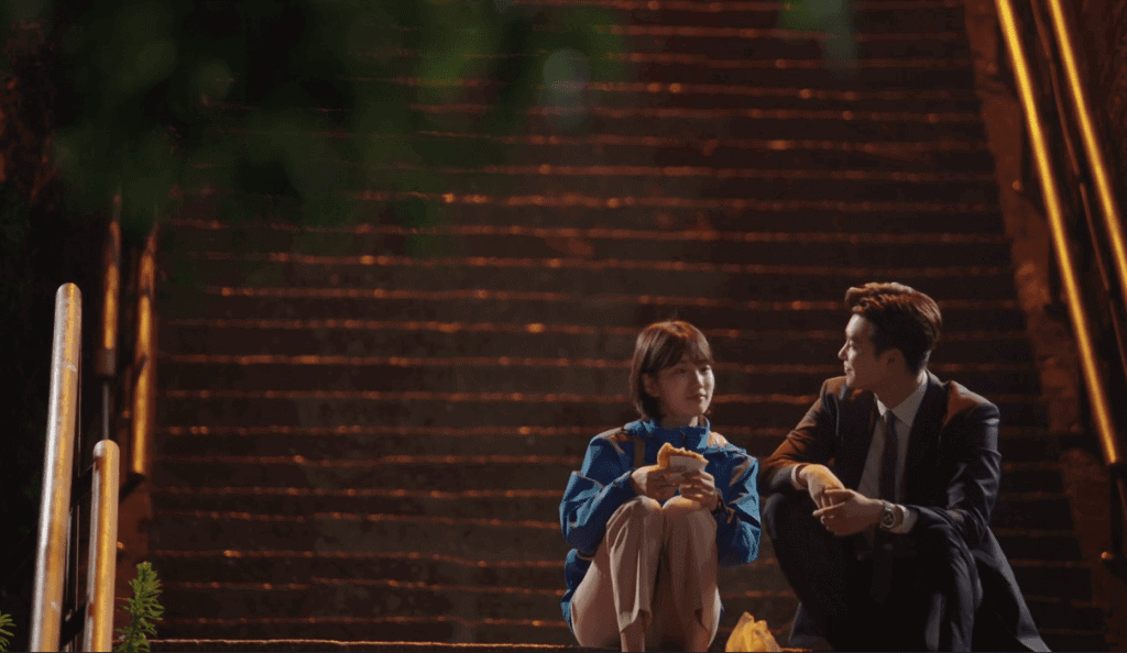 Nam Hong-Joo and Jung Jae-Chan sitting on some steps at right, talking.