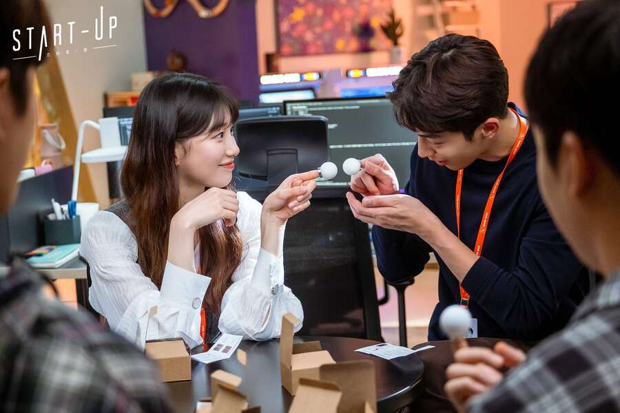 Seo Dal-mi and Nam Do-san with round objects on their index fingers, reaching to connect the round objects while smiling cutely